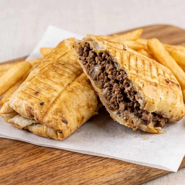 Grilled beef and cheese panini, cut in half, served with golden french fries on a wooden board.