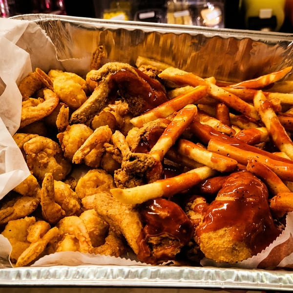 A large foil tray of fried shrimp, chicken, and french fries with barbecue sauce.