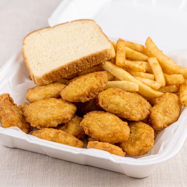 A white takeout container filled with golden-brown chicken nuggets, french fries, and a slice of white bread.